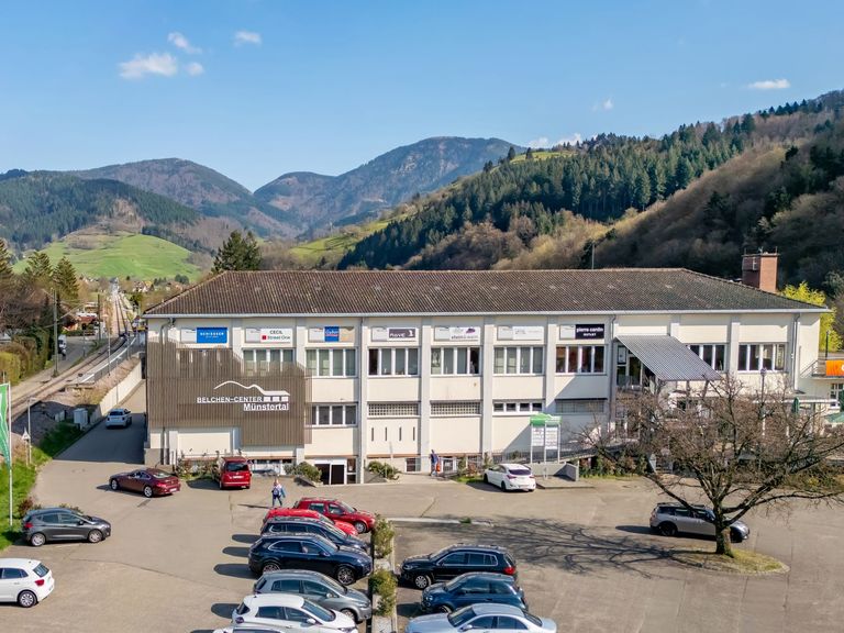 Das Belchen-Center mit Parkplatz vor bewaldeten Schwarzwaldhängen in Münstertal